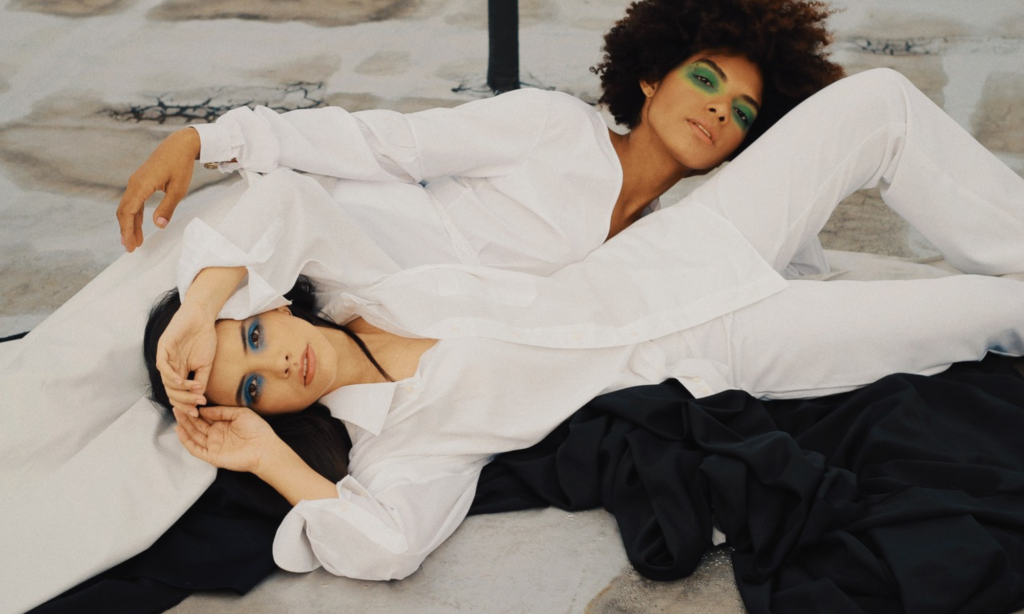 Two women lying opposite each other, both dressed in white shirts and trousers