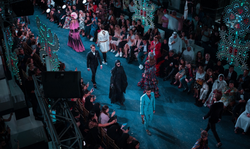 Men and women going down a blue runway in a fashion show