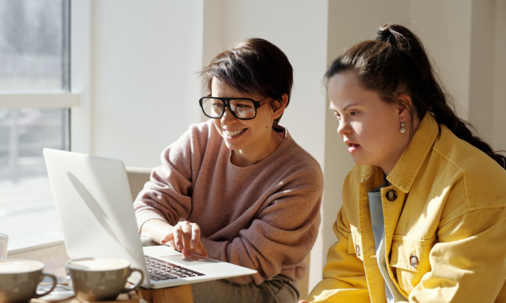 A woman showing another woman with Down syndrome something on a laptop