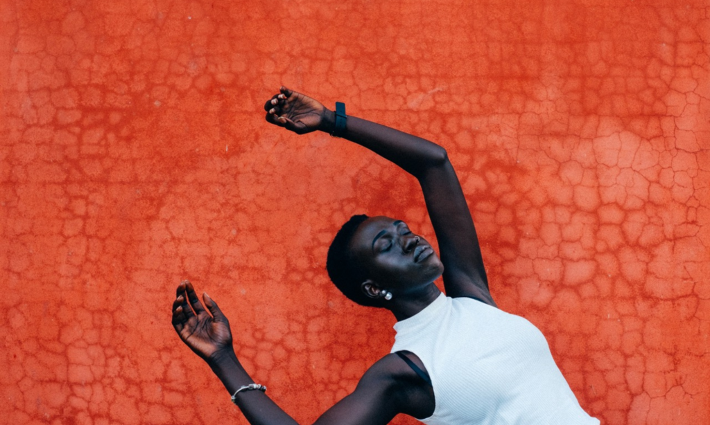 Black women posing with her hands up and her eyes closed with an orange background